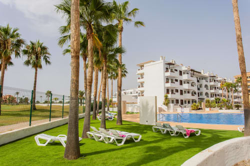 Lush green lawn with white loungers, palm trees, and pool at Haus Holiday Homes in San Pedro del Pinatar