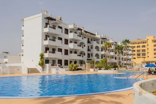 Large resort pool with white apartment buildings and palm trees at Haus Holiday Homes in San Pedro del Pinatar