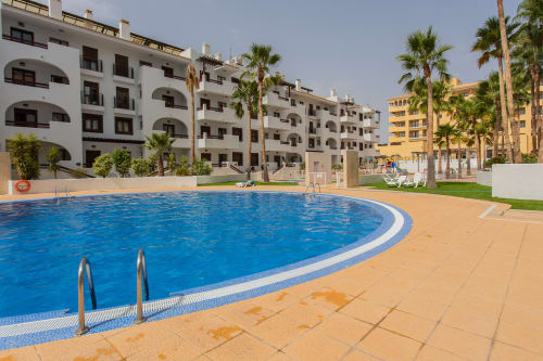 Curved swimming pool with palm trees and white apartment buildings at Haus Holiday Homes in San Pedro del Pinatar, Spain