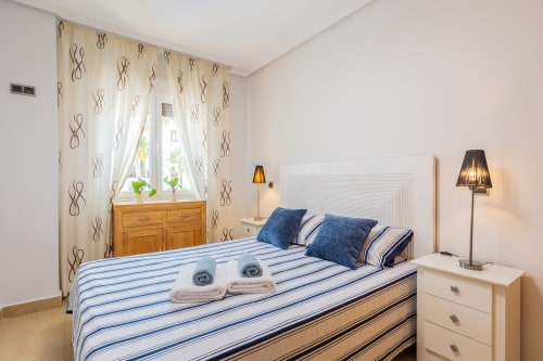 Bright bedroom at Haus Holiday Homes in San Pedro del Pinatar with blue striped bedding, white headboard, wooden furniture,