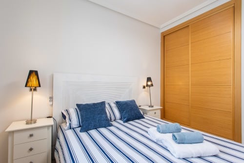 Modern bedroom with blue striped bedding, white headboard, wooden wardrobe, and bedside lamps at Haus Holiday Homes, San