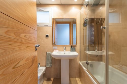 Modern bathroom in Alfa Living apartment at Haus Holiday Homes with pedestal sink, mirror, and glass shower enclosure