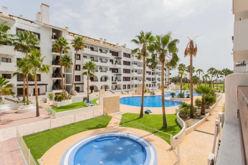 White apartment complex with palm trees, blue pool, and green grounds in San Pedro del Pinatar
