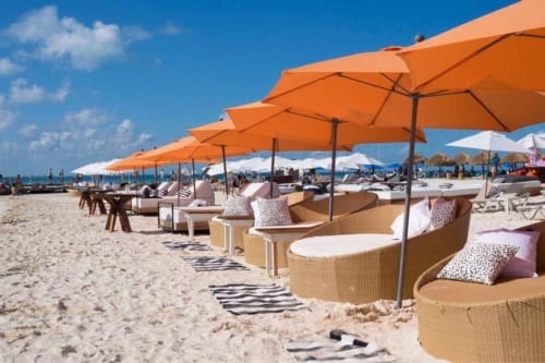 Beachfront lounge area at Malkita Homes in Isla Mujeres with orange umbrellas, woven seating, and ocean view on white sand.