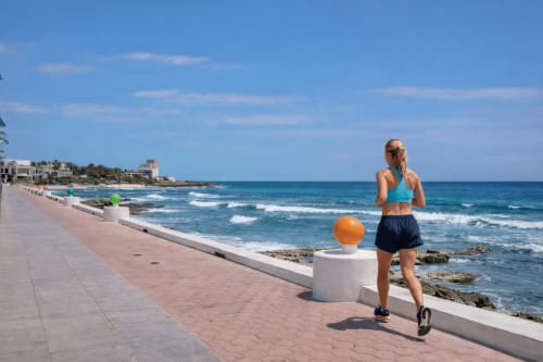Woman jogging on beachfront promenade with ocean waves and Isla Mujeres coastline in background