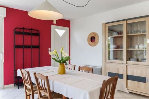 Salle à manger lumineuse du gîte Les Petits Toits à Libourne avec mur d'accent rouge, chaises en bois et lumière naturelle