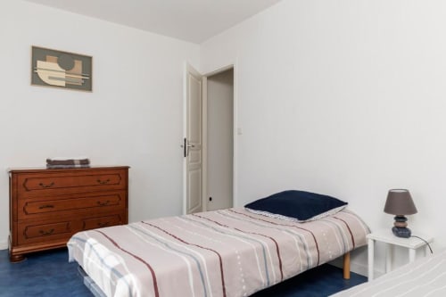 Chambre lumineuse du gîte Les Petits Toits à Libourne avec literie rayée, commode en bois et vue sur le jardin
