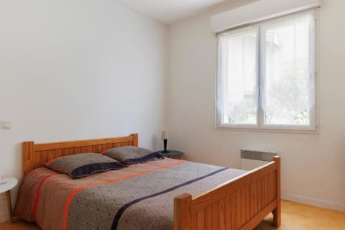 Chambre lumineuse avec lit en bois, literie grise et orange, grandes fenêtres vue sur jardin, gîte Les Petits Toits, Libourne