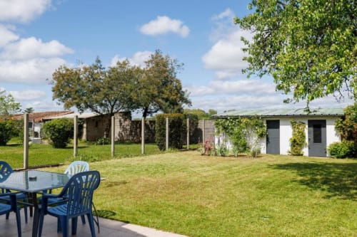 Jardin spacieux du gîte Les Petits Toits à Libourne avec coin détente bleu, pelouse soignée et arbres ombragés