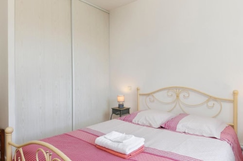 Chambre lumineuse au gîte Les Petits Toits à Libourne avec lit orné, literie rayée rose, oreillers blancs et grande