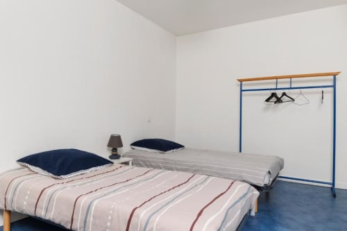 Chambre minimaliste à la gîte Les Petits Toits à Libourne avec literie rayée, oreillers bleu marine et portant à vêtements