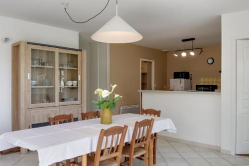 Salle à manger spacieuse du gîte Les Petits Toits à Libourne avec chaises en bois, nappe blanche et luminaires suspendus