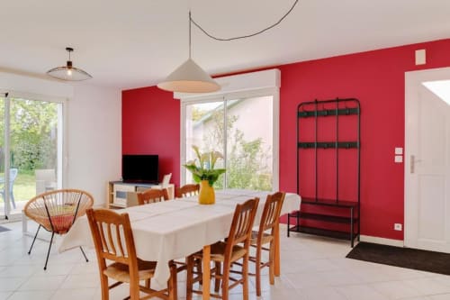 Salle à manger contemporaine du gîte Les Petits Toits à Libourne avec murs rouges, chaises en bois et vue sur le jardin