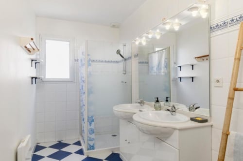 Salle de bain moderne avec doubles lavabos, grand miroir éclairé et douche vitrée au gîte Les Petits Toits