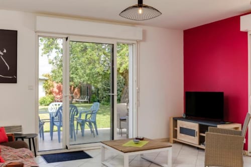 Séjour lumineux avec mur d'accent rouge, téléviseur et portes vitrées donnant sur la terrasse du jardin - gîte Les Petits Toits à Libourne