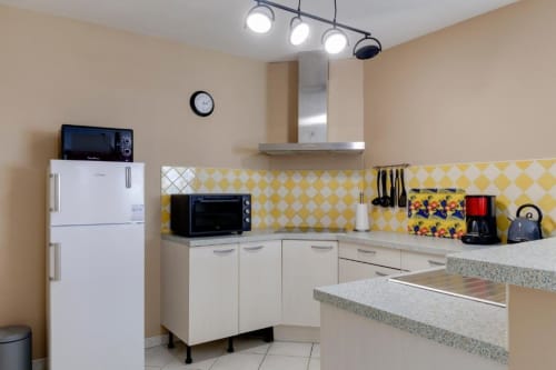Cuisine chaleureuse aux Petits Toits : carrelage jaune losange, mobilier blanc et appareils inox