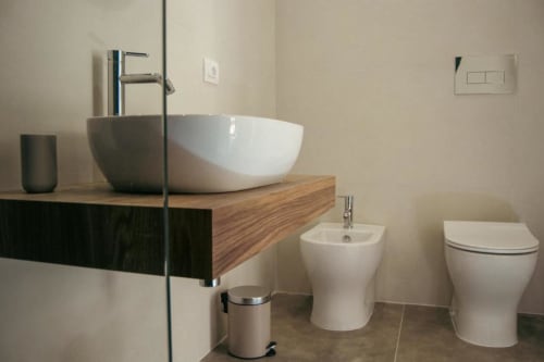 Bagno moderno nella Olive Tree Room del Baglio Capo con lavabo bianco, bidet, WC e vanità in legno