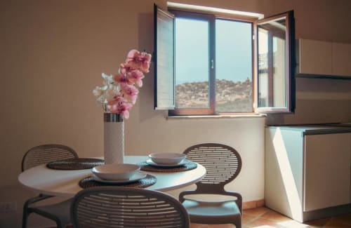 Elegante zona pranzo della suite Rosmarino al Baglio Capo con tavolo rotondo, sedie intrecciate, orchidee rosa e vista lago