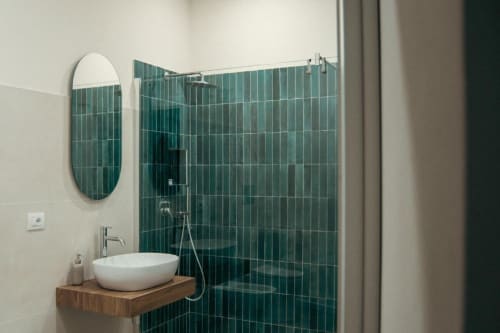 Bagno moderno nella Stanza Bougainville del Baglio Capo a Siculiana, con doccia in piastrelle verdi, lavabo bianco e specchio rotondo