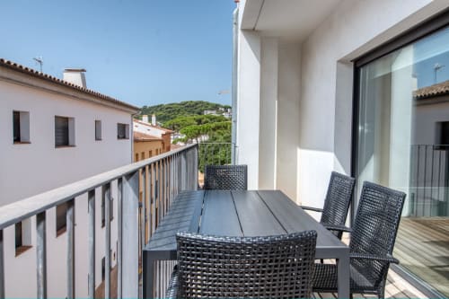 Modern apartment balcony in Calella with dining table, black wicker chairs, and hillside views of Palafrugell