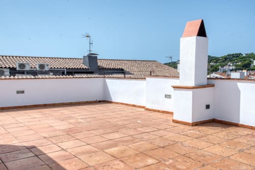Sunny rooftop terrace of Finques Garcia Enrich duplex in Calella, Palafrugell with terracotta tiles and white walls