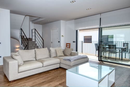 Modern duplex living room in Calella with beige sectional sofa, glass coffee table, and terrace access