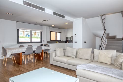 Modern duplex apartment in Calella with open-plan living, cream sofa, dining area, kitchen, and staircase in Palafrugell