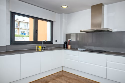 Modern white kitchen with gray countertops, stainless steel appliances, and window view in Calella apartment