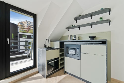 Modern kitchenette in Mattbnb Metz room with stove, sink, shelving and city view through glass door