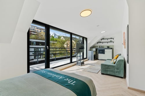 Modern bedroom in Metz with city views, green accent chair, kitchenette, and black-framed balcony doors at Mattbnb Ankoni