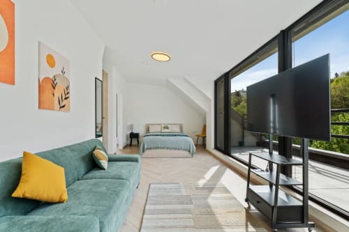 Modern bedroom at Mattbnb Metz with teal sofa, city views through glass doors, TV, and contemporary décor
