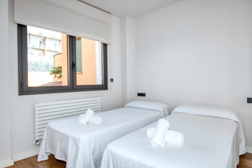 Twin bedroom with white linens and rolled towels, modern window with dark frame overlooking Calella, radiator heating in