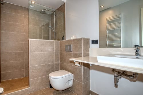 Modern bathroom in Calella apartment with walk-in shower, white toilet, heated towel rack, and dual sink vanity