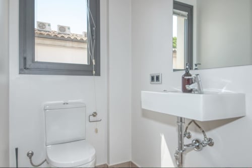 Modern bathroom with white sink, toilet, mirror and window at Finques Garcia Enrich apartment in Palafrugell