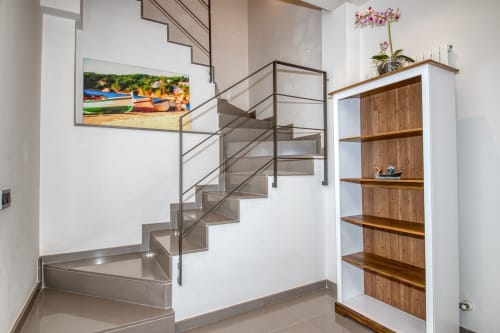 Modern duplex staircase with metal railings, wooden shelving, and coastal artwork in Calella apartment