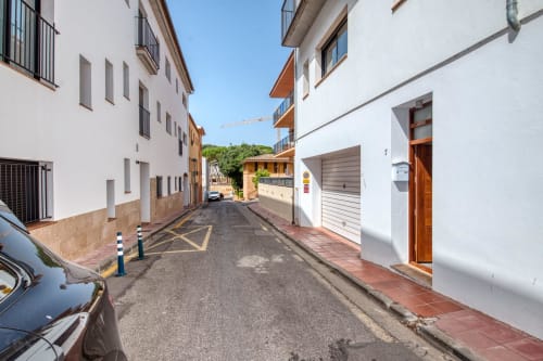 Narrow residential street in Palafrugell with white buildings, parked cars, and colorful doors leading to apartment