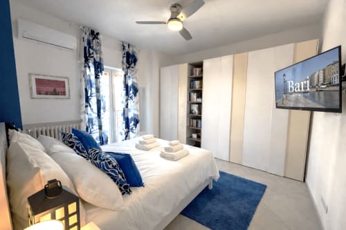 Camera moderna agli Appartamenti Bari con biancheria bianca, dettagli blu, TV a schermo piatto e vista sulla città di Bari, Italia