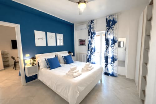 Camera moderna agli Appartamenti Bari con parete blu, letto bianco, tende bianche e blu, e vista sulla città di Bari, Italia