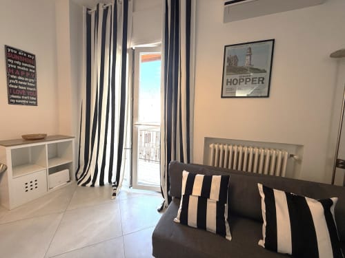Elegante soggiorno moderno con divano scuro, cuscini rigati e balcone arredato con vista sulla città di Bari