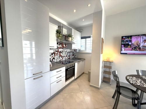 Cucina moderna negli Appartamenti Bari con mobili bianchi, piano di lavoro nero, zona pranzo e TV a Bari, Italia