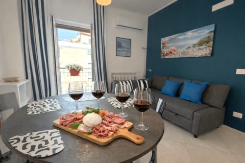 Soggiorno moderno a Bari con parete azzurra, divano grigio, tavolo con tagliere di salumi e calici di vino