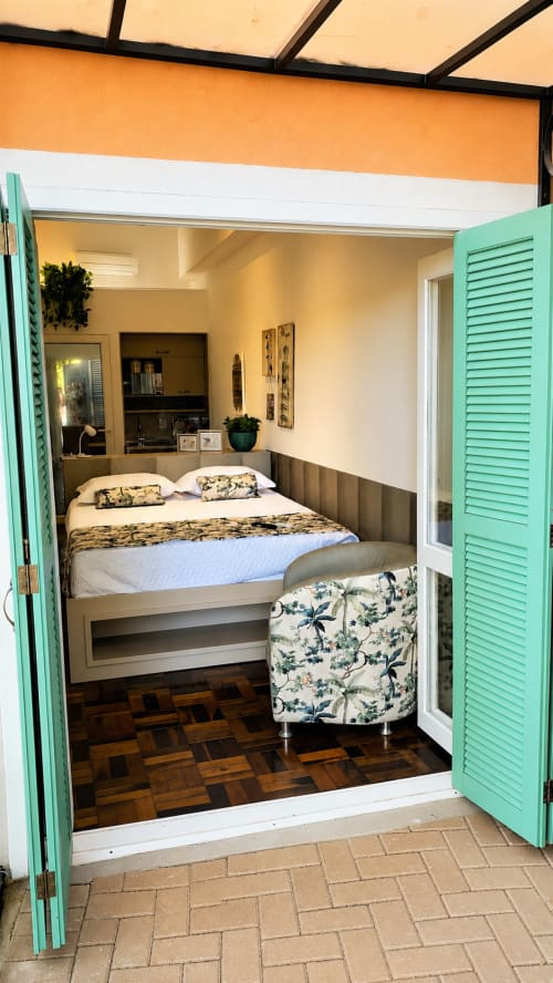 Quarto aconchegante em loft em Maringá com portas turquesas, cama queen, área de trabalho, piso de madeira e vista para o jardim