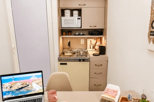 Kitchenette aconchegante em loft em Maringá com fogão compacto, pia, micro-ondas e espaço de trabalho com laptop