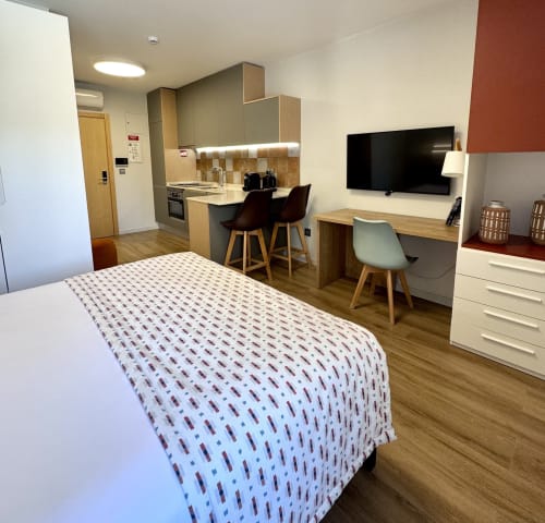 Studio moderno no RIA CENTRUM Smart Residence em Aveiro com cama, cozinha, área de refeições, TV e espaço de trabalho