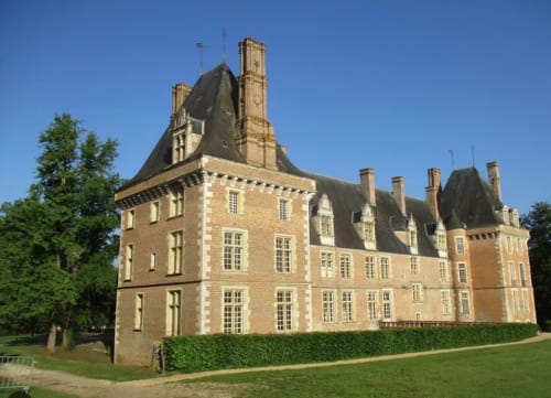 Domaine de l'Ocrerie, a grand brick château with mansard roofs in Pourrain, France, surrounded by manicured gardens.