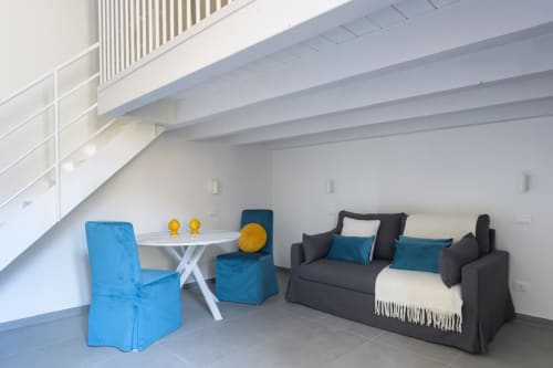 Appartamento Blu Ottanio dell'hotel Almatros a Sulmona con sedie blu, tavolo bianco e divano scuro con accenti teal