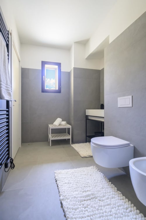 Bagno moderno nell'appartamento Blu Ottanio dell'hotel Almatros a Sulmona con piastrelle grigie, finestra con cornice blu e design contemporaneo