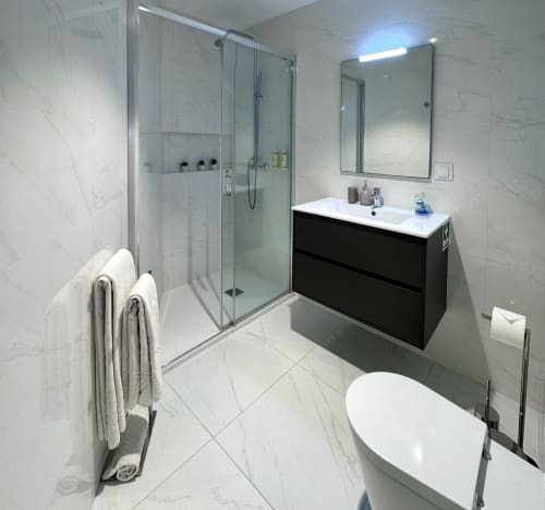 Salle de bain moderne au RIA CENTRUM Smart Residence à Aveiro avec carrelage marbre, douche vitrée, meuble vasque noir et sèche-serviettes électrique