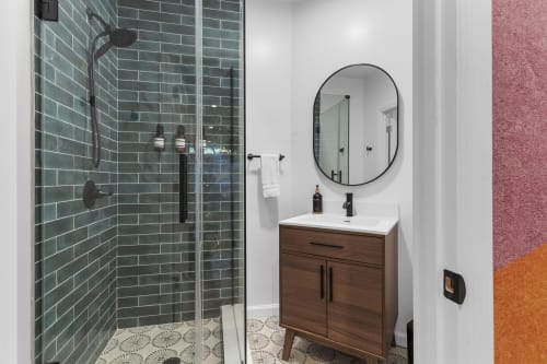 Modern bathroom at Malkita Terra villa in Woodbury with green tile shower, round mirror, and wood vanity