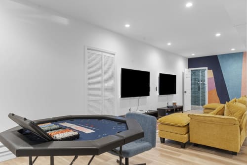 Game room in Malkita Terra villa, Woodbury with poker table, pool table, TVs, yellow seating, and colorful accent wall